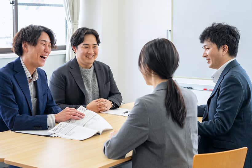 白衣の社員が部品について説明している様子